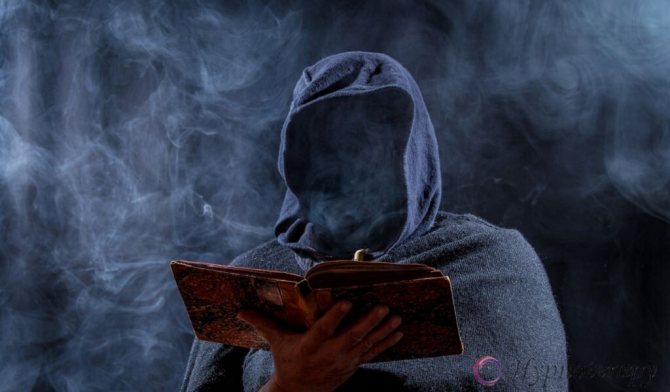 Человек скрывающий своё лицо за капюшоном, держит в руках раскрытую книгу