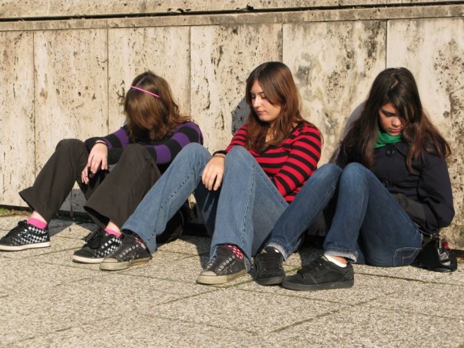 Девочки-подростки сидят на тротуаре