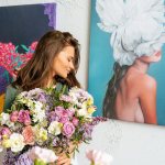 Девушка с букетом цветов на фоне висящей на стене современной живописи