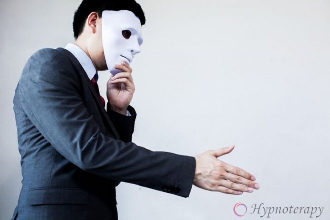 Молодой человек в костюме скрывает лицо за белой маской протягивает руку