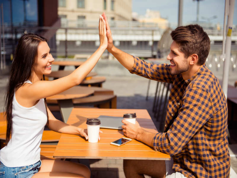 парень с девушкой дают пять сидя за столом в кафе