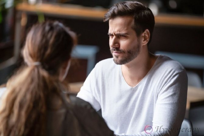 Сомневающийся недовольный мужчина, подозрительно смотрит на женщину во время их разговора за столом в кафе