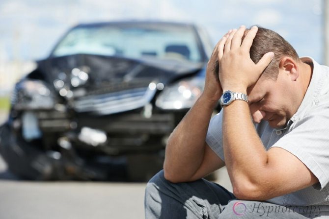 Взрослый мужчина сидит схватившись за голову на фоне разбитого автомобиля на городской трассе