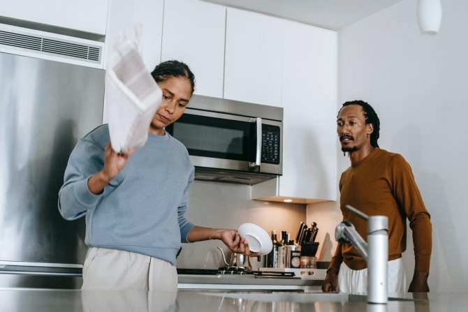 Женщина с недовольным лицом стоит на кухне рядом с мужчиной
